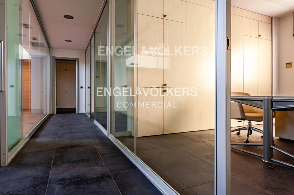 Office space with glass-walled rooms, dark tile floors, and Engel & Völkers Commercial logo on the glass.