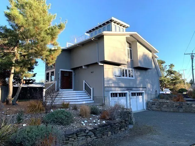 Exterior view of a modern, multi-level gray house with white trim, a two-car garage, and a landscaped front yard.