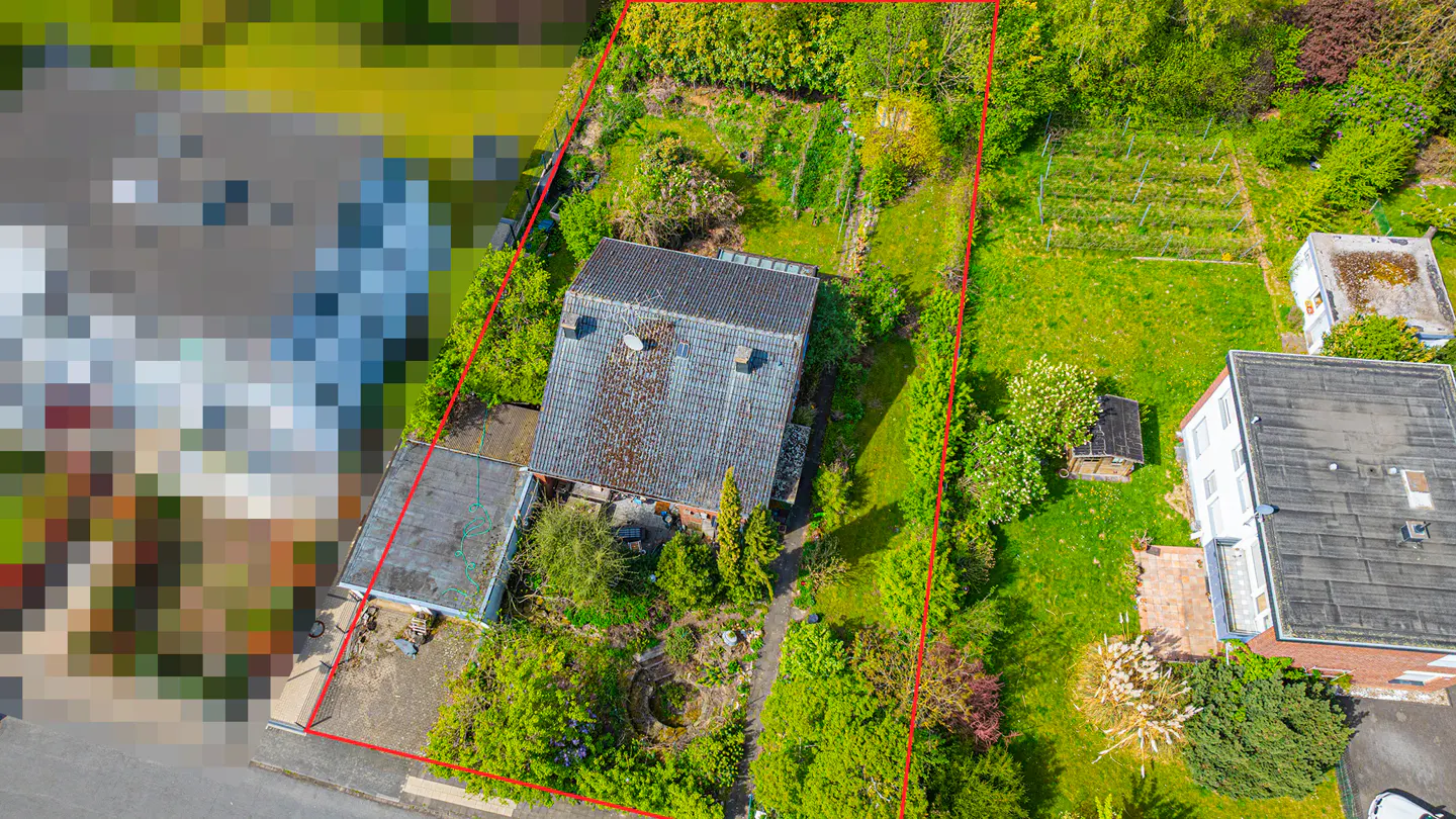 Aerial view of a house with a gray roof, surrounded by green trees and grass, marked with a red boundary line.