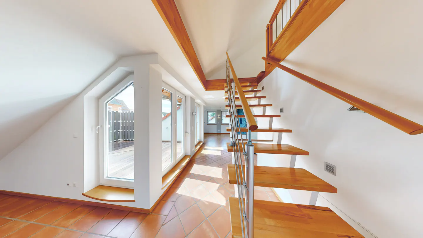 Bright hallway with wood stairs and terracotta tile floor. White walls and large windows lead to a balcony.