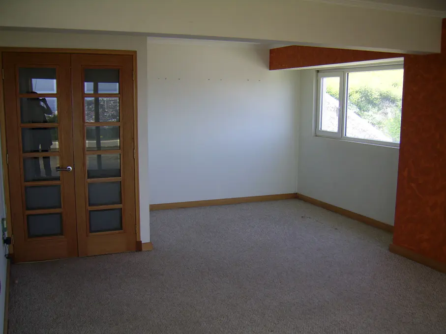 Empty room with beige carpet, white walls, and wood trim. Double doors with glass panes and a window with a view of greenery.