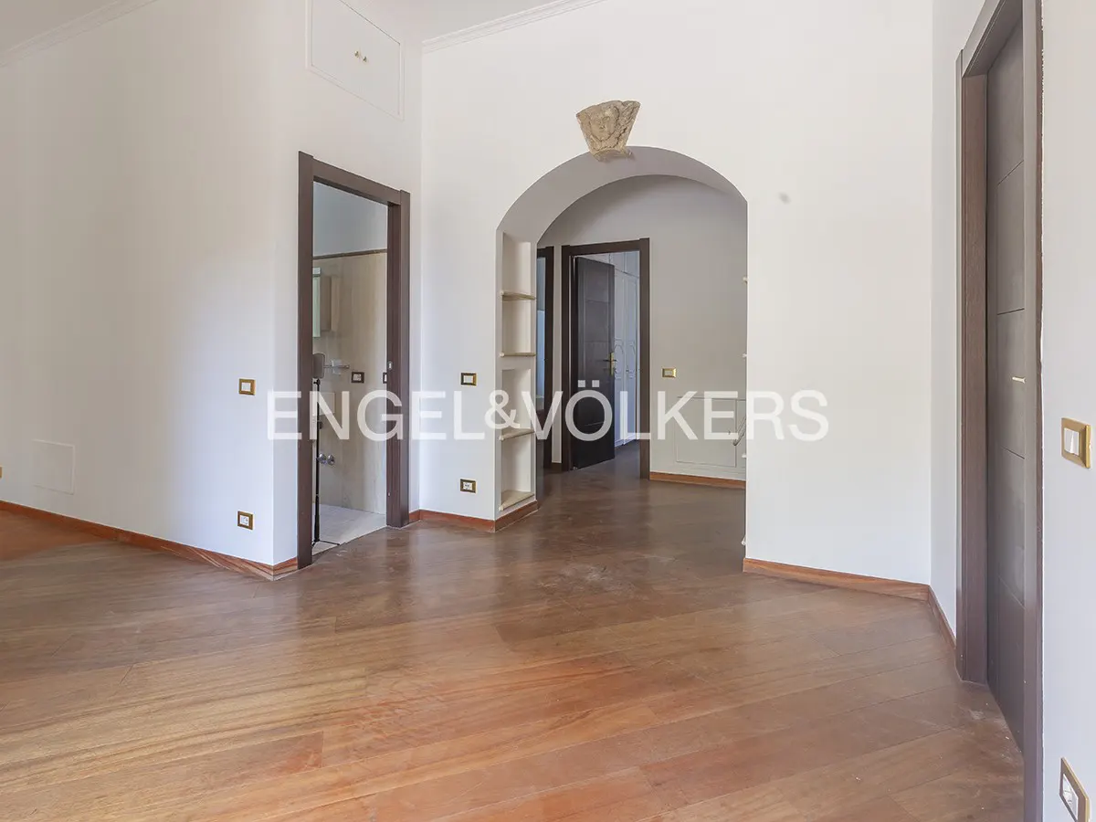 Empty room with hardwood floors, white walls, and dark wood trim. Archway leads to another room. Engel & Völkers logo visible.
