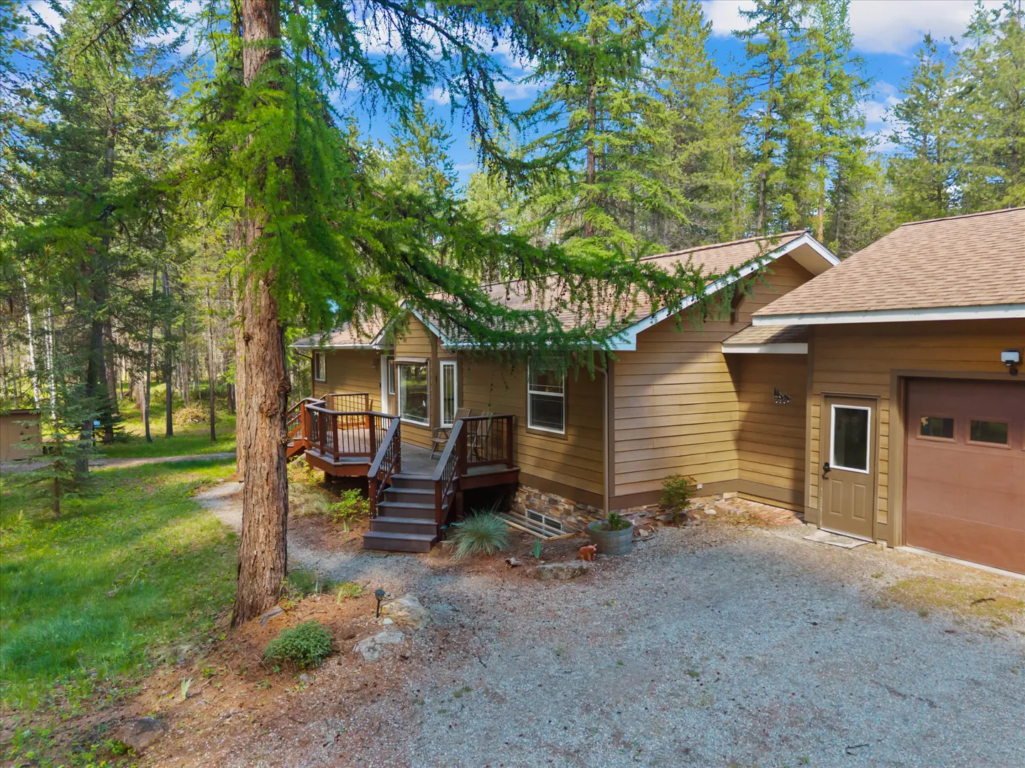 A tan house with a brown roof and a brown garage door is surrounded by green trees.