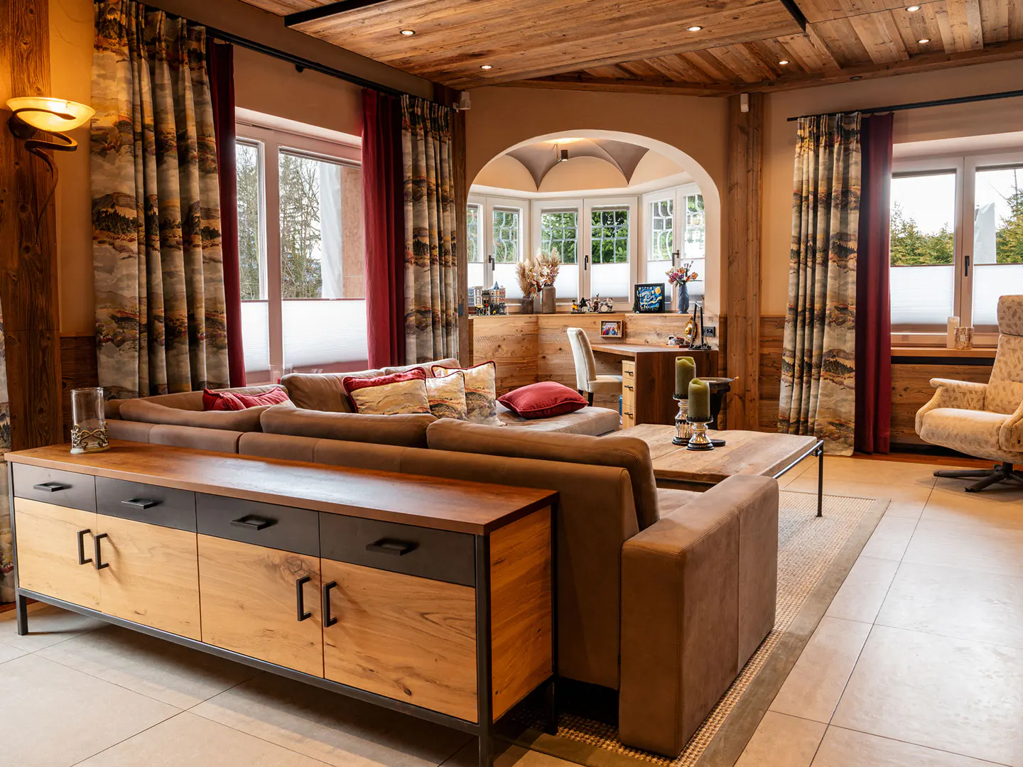 Living room with wood paneled ceiling, brown sofa, wood cabinet, and bay window with desk.