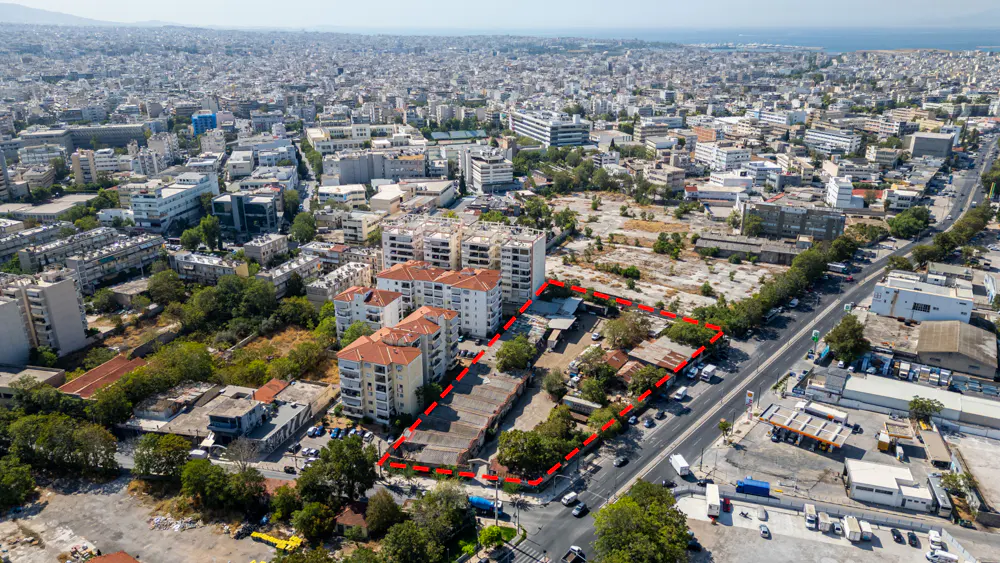 Aerial view of a property outlined in red, surrounded by buildings, trees, and a city skyline.